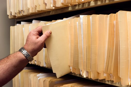 Human Hand Pulls File Folder off Shelf of Client Files
