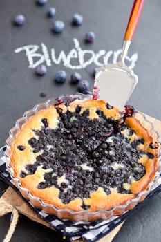 Blueberry pie in glass dish and server with word blueberry written in chalk on dark background