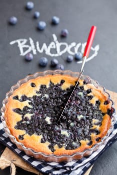 Blueberry pie in glass dish and server with word blueberry written in chalk on dark background
