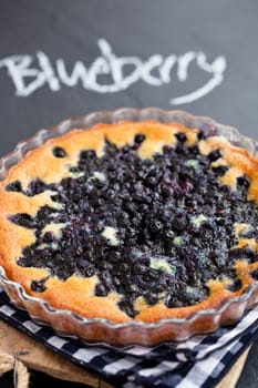 Closeup of blueberry pie in glass dish with word blueberry written in chalk on dark background
