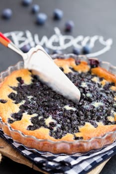 Closeup of lueberry pie in glass dish and server with word blueberry written in chalk on dark background