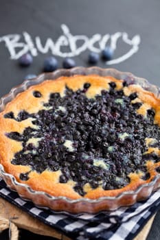 Closeup of blueberry pie in glass dish with word blueberry written in chalk on dark background