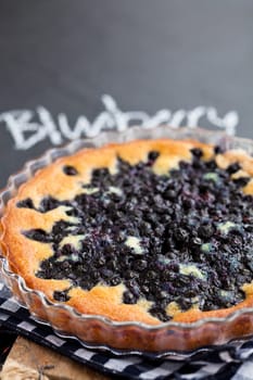 Closeup of blueberry pie in glass dish with word blueberry written in chalk on dark background