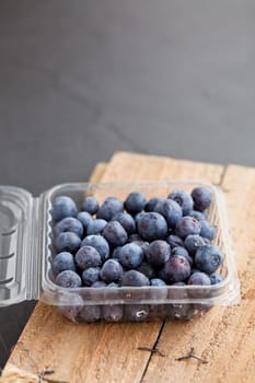 Closeup of fresh blueberries in plastic container resting on wooden serving surface