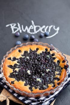 Blueberry pie in glass dish with word blueberry written in chalk on dark background