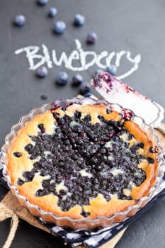 Blueberry pie in glass dish and server with word blueberry written in chalk on dark background