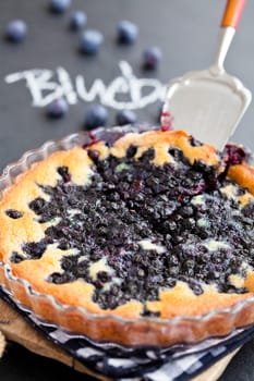 Closeup of blueberry pie in glass dish and server with word blueberry written in chalk on dark background