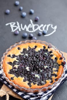 Blueberry pie in glass dish with word blueberry written in chalk on dark background