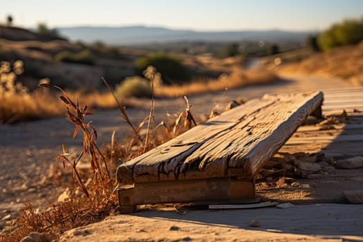 an old wooden bench on the side of a dirt road with mountains in the distance and grass growing up to the ground