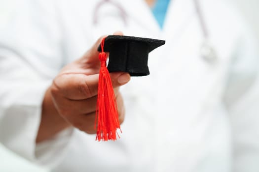 Asian woman doctor holding graduation hat in hospital, Medical education concept.
