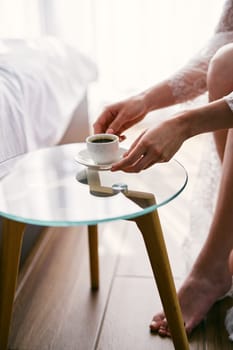 Bride takes a cup of coffee from a glass table while sitting in an armchair. Cropped. Faceless. High quality photo