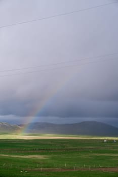 Rainbow on a sunny plain against the backdrop of mountains and stormy skies. High quality photo