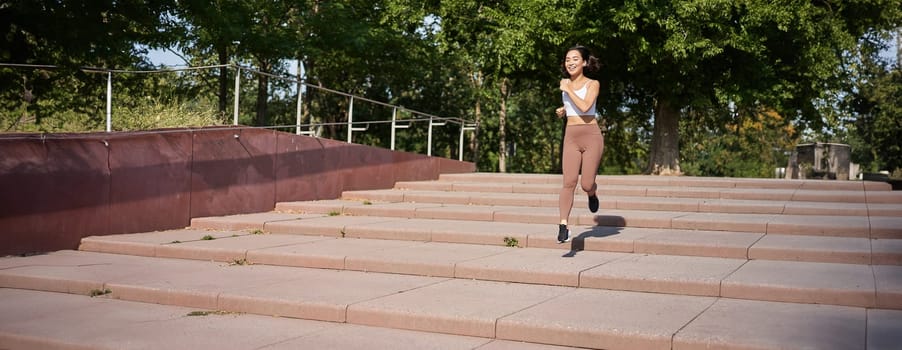 Healthy fitness girl running outdoors on street, wearing uniform, jogging on fresh air and listening music in wireless headphones.