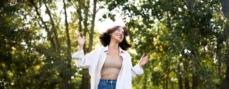 Happy people. Carefree asian girl dancing and enjoying the walk in park, feeling happiness and joy, triumphing.