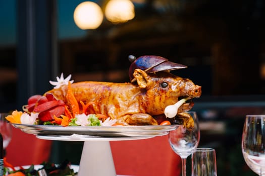 Roasted pig garnished with colorful vegetables lies on a platter on the table. High quality photo