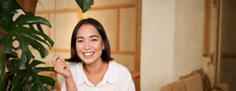 Stylish young woman in cafe with coffee, holding mobile phone, laughing and smiling. Lifestyle and people concept.