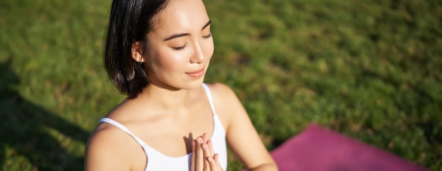 Portrait of young mindful woman, practice yoga, exercising, inhale and exhale on fresh air in park, sitting on rubber mat.