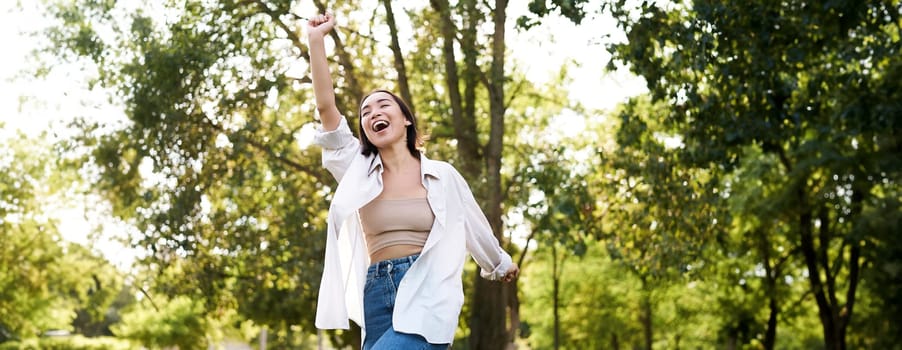 Happy people. Carefree asian girl dancing and enjoying the walk in park, feeling happiness and joy, triumphing.