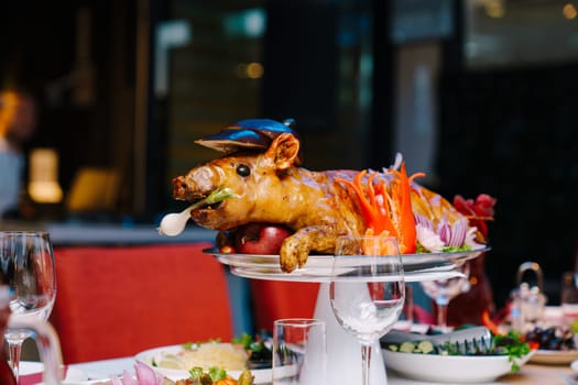 Roasted pig garnished with vegetables lies on a dish on a table in a restaurant. High quality photo