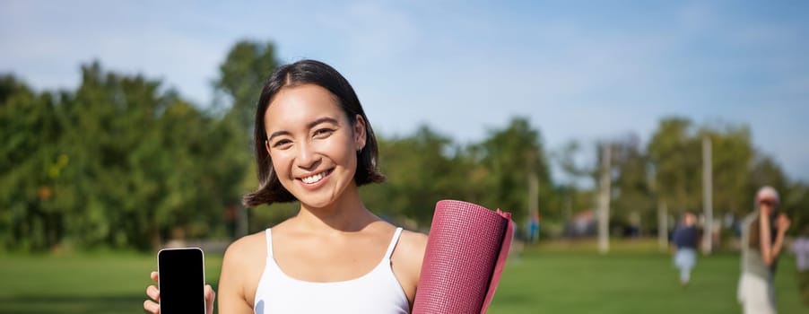 Vertical shot of fit and healthy young asian woman, shows smartphone screen with her workout stats, recommends telephone application.