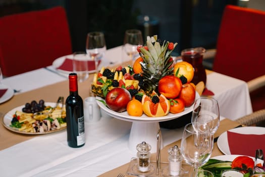 Fruit platter stands on the festive table next to wine and snacks. High quality photo