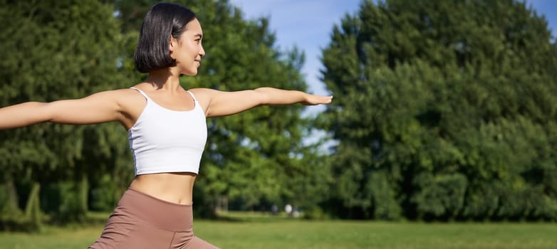 Young woman stretching her body, workout and doing yoga in park, standing on rubber mat in fitness clothing during training session.