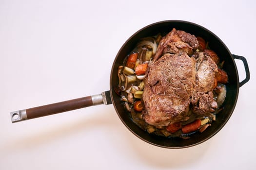 Frying pan with a wooden handle with roast beef and vegetables on a white table. Top view. High quality photo