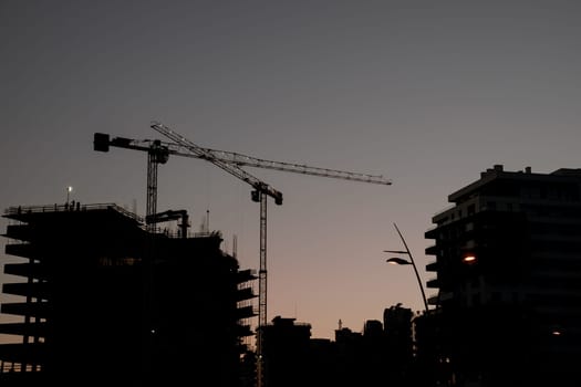 High tower cranes work on the construction site of high-rise buildings with illumination at sunset. High quality photo