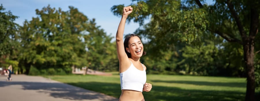 Hooray, victory. Smiling asian girl triumphing, celebrating achievement, running till finish, shouting from excitement.