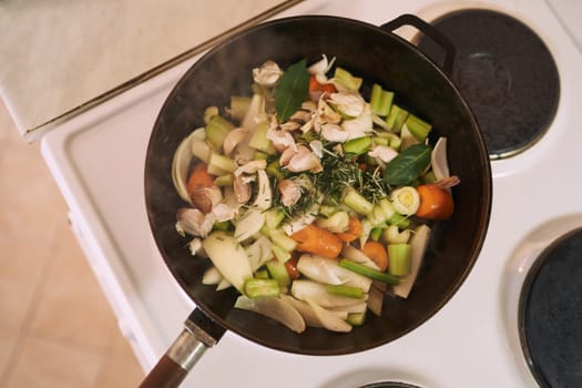 Raw chopped vegetables are stewed in a frying pan on the stove. Top view. High quality photo