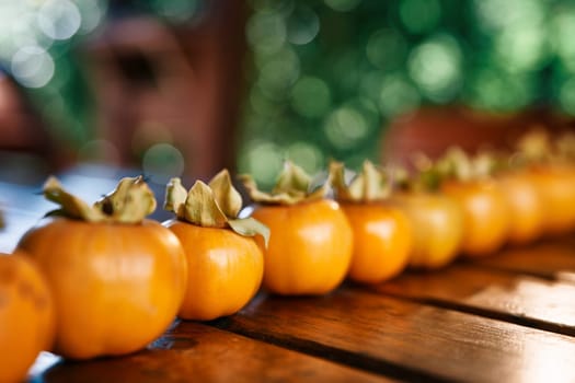 Yellow large persimmons, lined up in a row, lie on a wooden table. High quality photo