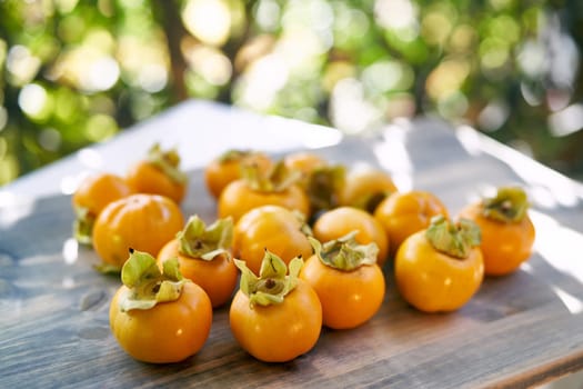 Juicy orange persimmons lie on a wooden table on the balcony in the sunlight. High quality photo