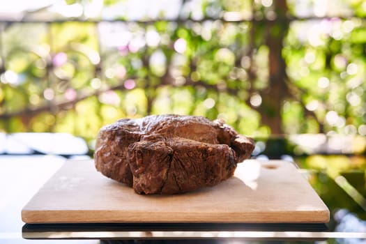 Roast beef lies on a wooden cutting board on the table in the sun. High quality photo