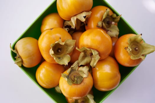 Full rhombic bowl of orange persimmons on a white table. Top view. High quality photo
