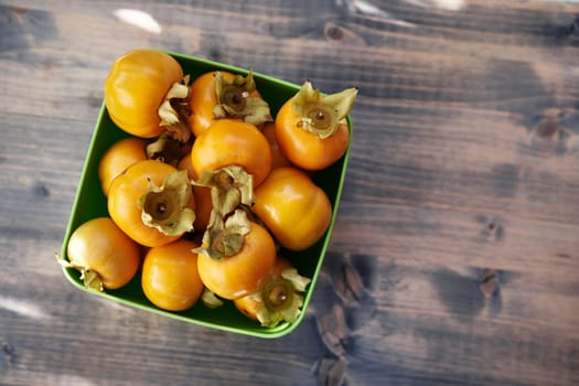 Rectangular bowl with ripe persimmons stands on a wooden table. Top view. High quality photo