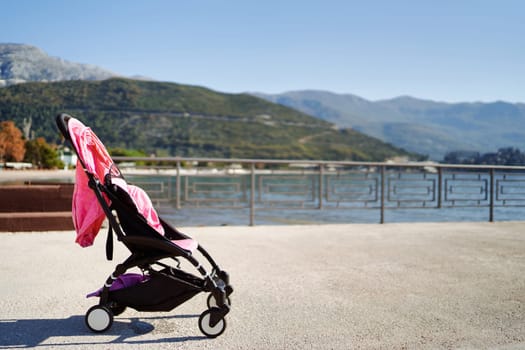 Baby stroller stands on the coast of the sea against the backdrop of mountains. High quality photo