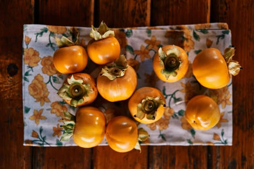 Ripe persimmons are laid out on a colorful napkin on a wooden table. Top view. High quality photo