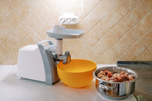 Electric meat grinder stands on a table next to a bowl and a pot of minced meat. High quality photo
