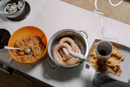 Bowl of minced meat stands near an electric meat grinder making sausage in the kitchen. High quality photo