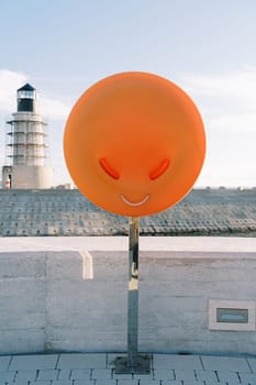 Lifebuoy in an orange box on the pier against the background of the lighthouse. High quality photo