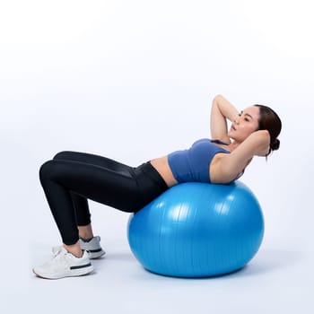 Young attractive asian woman portrait in sportswear with fit ball targeting on abs muscle for effective energetic daily workout routine. Studio shot and isolated background. Vigorous