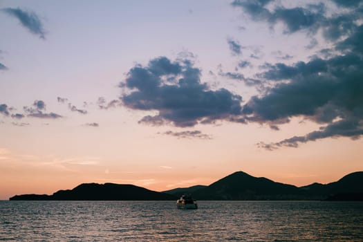 Motor yacht sails on the sea towards the mountains at sunset. High quality photo