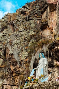 Statue of the Virgin Mary with a dramatic cliff rising behind it
