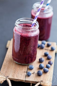 Closeup of blueberry smoothies in glasses with striped straws on wooden serving tray with blueberries