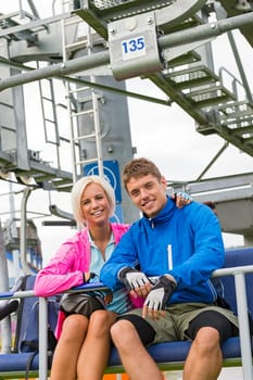 Smiling couple in sweatsuit sitting on char lift in springtime