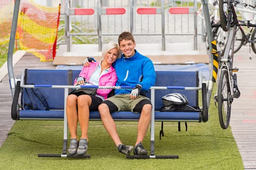 Cuddling happy couple sitting on chair lift with bicycles