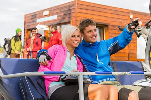 Cheerful couple sitting on chair lift man pointing