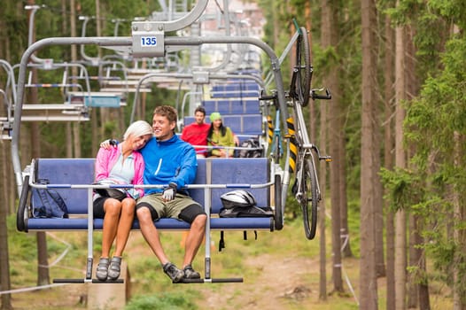 Carefree couple traveling by chair lift with bicycle