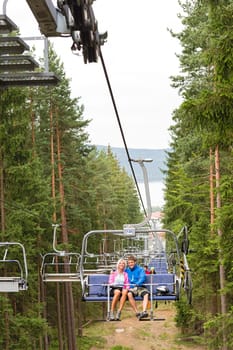 Young couple sitting on chair lift traveling through forest