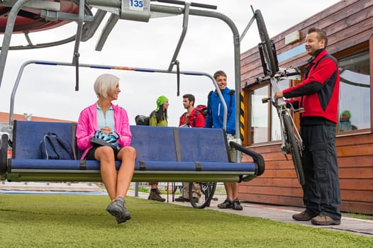 Happy couple sitting on chair lift man securing bicycle